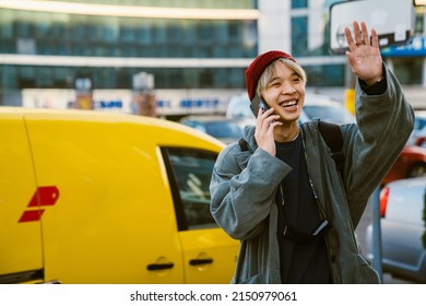 Asian Boy Laughing And Gesturing While Talking On Mobile Phone At City Street