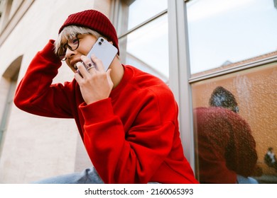 Asian Boy Laughing And Talking On Mobile Phone By Wall Outdoors