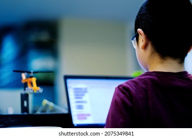 Asian Boy Learning Computer Programming In Front Of Laptop. He Is Working On His Robotics Project And Developing Robot Model. Child Science, Coding, Robotics And STEM Education Background.