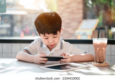 Asian Boy Learning Online In Cafe Alone. Son Relax With Play Game On Smartphone.