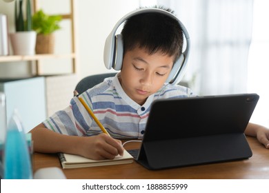 Asian boy learning online via internet with a tutor on a tablet digital with headphone, Asia child is studying while sitting in the living room at home. Concept of online learning at home  - Powered by Shutterstock