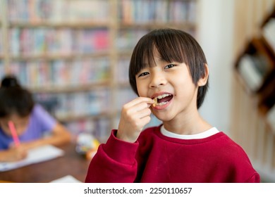 Asian boy look like Chinese enjoy with eating candy in classroom while his friend concentrate in drawing or painting work. - Shutterstock ID 2250110657