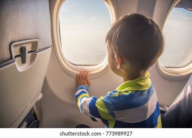 Asian Boy Looking Aerial View Of Sky And Cloud Outside Airplane Window While Sitting On Airplane Seat.