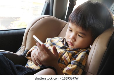 Asian Boy Looking At Smartphone Screen. Child Sitting On Car Seat And Watch Video Cartoon On Mobile Phone. Kid Holding Cellphone In His Hand.