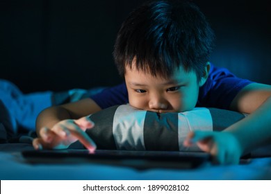 Asian boy lying in bed at night and playing digital tablet. Soft focus image. - Powered by Shutterstock