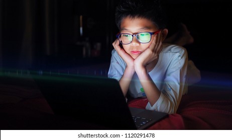 Asian boy lying in bed and watching laptop at night.