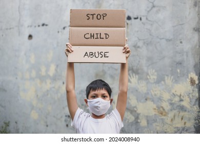 Asian boy in medical mask raising letter board says Stop Child Abuse  campaign with hand print in the cement wall background