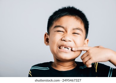 Asian boy missing front tooth illustrates dentistry and health care pointing to gap. Conceptual image isolated on white background emphasizing dental growth and care. teeth new gap, dentist problems