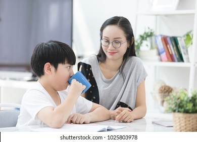 Asian Boy With Mother Teaching And Learning Your Homework At Home ,Boy Drink A Glass Of Milk .