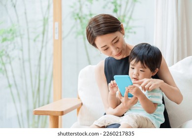 asian boy and mother using smart phone in the living room - Powered by Shutterstock