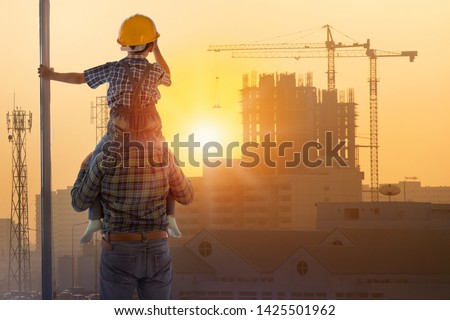 Asian boy on father's shoulders with background of new high buildings and silhouette construction cranes of evening sunset, father and son concept