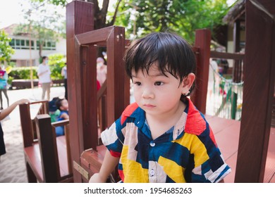 Asian boy play at outdoor playground. During summer or spring. Child felt hot and sweaty on his face. Taking care of health of young kid in hot weather. Baby 2-3 year old. Children wear colorful dress