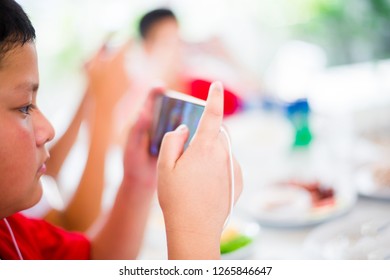 Asian boy play smartphone with earphone and friends for game and entertainment at dining table in restaurant - Shutterstock ID 1265846647