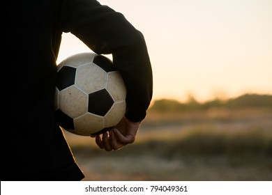 Asian boy player football soccer and holding ball in the meadow with sunset background