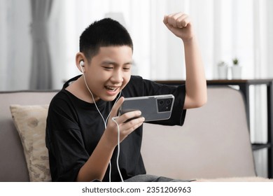 Asian boy playing games online with his smartphone, he feel fun and happy on a sofa, games addict problem - Powered by Shutterstock