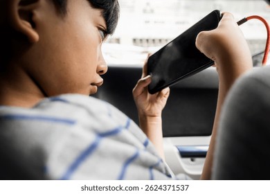 Asian boy playing online game on smartphone while being charged in full concentration inside of a car
