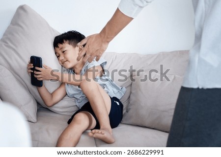 Asian boy refusing to give his smartphone to his father, showing signs of phone addiction and dependence on technology. Concept of family conflict, digital addiction.