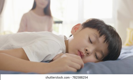 Asian Boy Sleeping In Bed In The Morning While Mother Sitting In Background