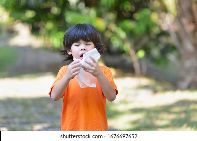 Asian boy sneezing into tissue paper.Child with orange shirt with influenza.Summer and spring allergy in outdoor.Young male with covid-19.Preschooler sneeze.Corona virus patient. - Powered by Shutterstock