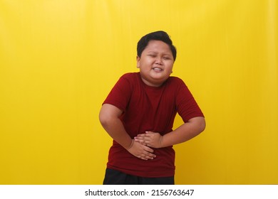 Asian Boy Standing Holding Stomach Feeling Hungry. Isolated On Yellow Background