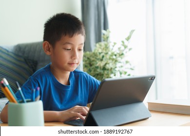 Asian Boy Is Studying Online Via The Internet On Tablet While Sitting In The Living Room In Morning, Asia Child Watching And Education Distance On The Computer. Concept Learning At Home