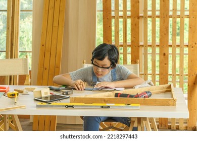 Asian Boy Is Studying Woodworking On Table With Various Tools Scattered About.