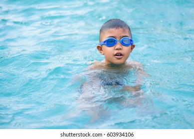 Asian Boy Swimming In The Outdoor Public Pool.Portrait Of Swimming Child With Goggles After Training In Water Pool.