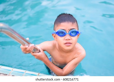 Asian Boy Swimming In The Outdoor Public Pool.Portrait Of Swimming Child With Goggles After Training In Water Pool.