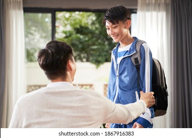 Asian boy talking to his father after school with paper in hand and backpack over shoulder