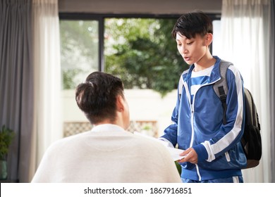 Asian Boy Talking To His Father After School With Paper In Hand And Backpack Over Shoulder 