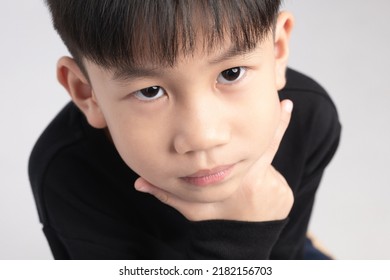 Asian Boy With Thinking Expression. A Kid About 6 Years Old Touching His Chin And Making Curious Face.