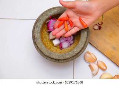 An Asian Boy  Is Using The Mortar And Pestle Or Lesung Batu In Malay With Crushed Chilies, Onions And Garlic For Cooking Rice Fried