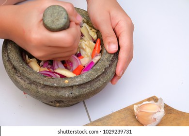 An Asian Boy  Is Using The Mortar And Pestle Or Lesung Batu In Malay With Crushed Chilies, Onions And Garlic For Cooking Rice Fried