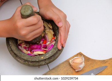 An Asian Boy  Is Using The Mortar And Pestle Or Lesung Batu In Malay With Crushed Chilies, Onions And Garlic For Cooking Rice Fried