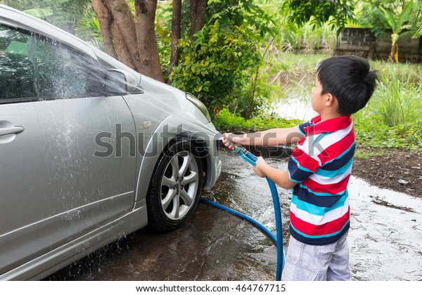 Asian\
boy washing car on water splashing in the\
garden.