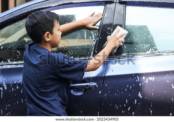 Asian boy washing a car  windows using sponge and\
soap foam
