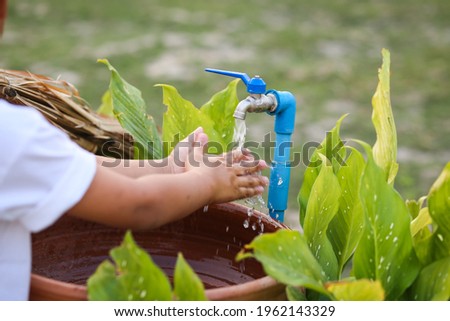 An Asian boy washing his hand at an outdoor faucet sink and water tab.