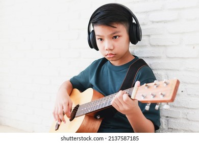 Asian boy wearing headphones with black music Sit and play guitar in the house. music learning concept, music proficiency training - Powered by Shutterstock