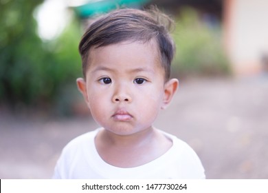 Asian Boy Wearing A White Shirt, Looking At The Camera, Not Smiling.