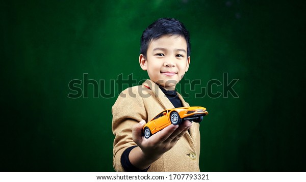 Asian Boys 5 years old, wearing a\
brown suit with a smile on his face He is carrying a yellow car on\
his hand.  He is happy every time when he plays this\
car.