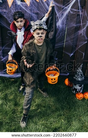 Asian boys in halloween costumes holding buckets with candies in backyard