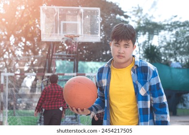 Asian boys in plaid shirt holding and playing basket ball with friends at outdoor basketball court of his school, soft focus, concept for freestyle and lifestyle of young teens around the world. - Powered by Shutterstock