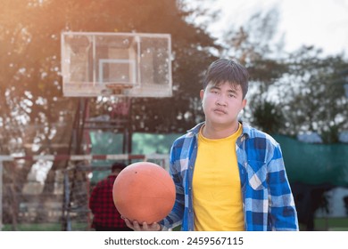 Asian boys in plaid shirt holding and playing basket ball with friends at outdoor basketball court of his school, soft focus, concept for freestyle and lifestyle of young teens around the world. - Powered by Shutterstock