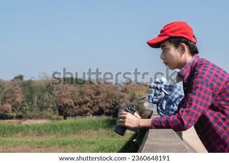 Asian boys using binoculars to do the birdwatching on bridge over the river in tropical forest during summer camp, idea for learning creatures and wildlife animals and insects outside the classroom.