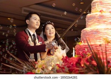 Asian Bride and Groom Holding a Knife and Cuting the Wedding Cake
