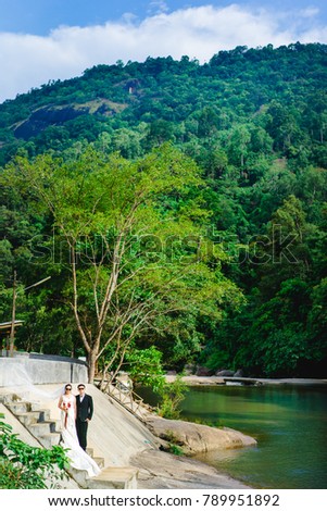 Asian bride and groom standing on the jungle and river at Village KHIRIWONG The best weather in Thailand.Bride and groom on a romantic moment in pure nature.