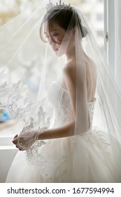 Asian bride in wedding dress by the window