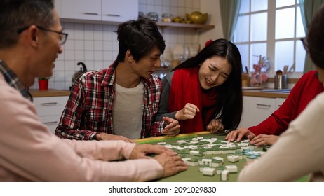 asian brother elbowed his sister out of chair while they are fighting at mahjong table. wagging finger refusing to give up on chinese new year. translation: luck