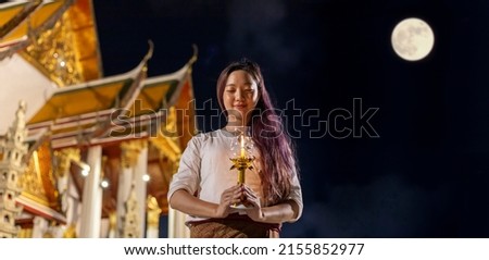 Asian buddhist woman lighting up the candle to pay homage to Lord Buddha on Vesak day at the full moon night inside golden temple for faith, belief and traditional religion culture