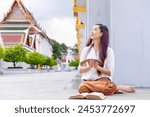 Asian buddhist woman is reading the Sanskrit ancient palm leaf manuscript of Tripitaka the Lord Buddha dhamma teaching while sitting in temple on holy full moon day to chant and worship in monastery